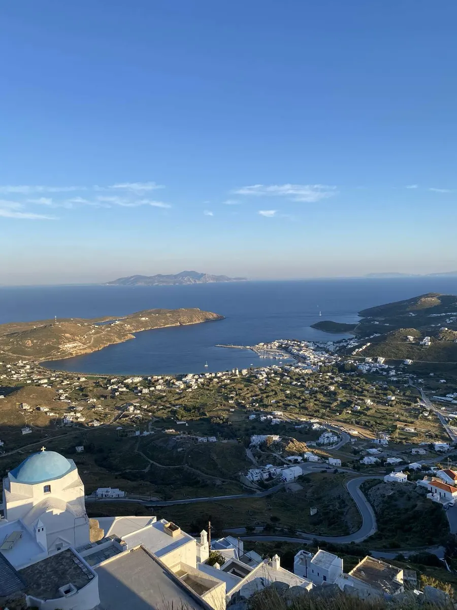 Cycladic bay and whitewashed village seen from above, blue chapel dome in the foreground, Greece