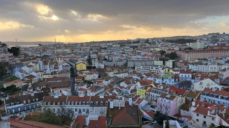 Lisbon rooftops at dusk from a viewpoint, the Tagus on the horizon